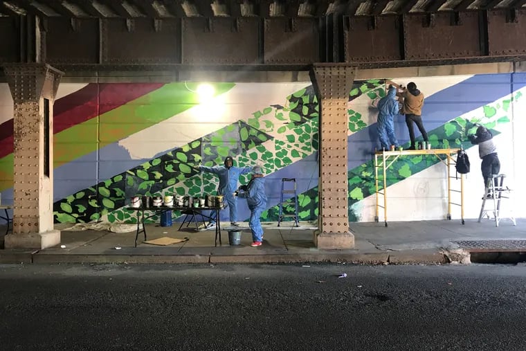 Participants in Mural Arts' day-labor program, Color Me Back, paint a mural on an underpass on Emerald Street in Kensington.