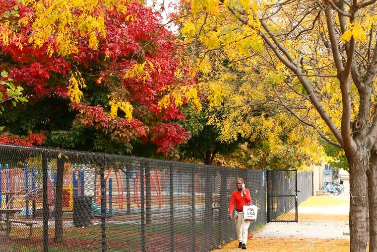 A pedestrian walks under trees changing colors to a fall foliage at the Hank Gathers Recreation Center in North Philadelphia late last October.
