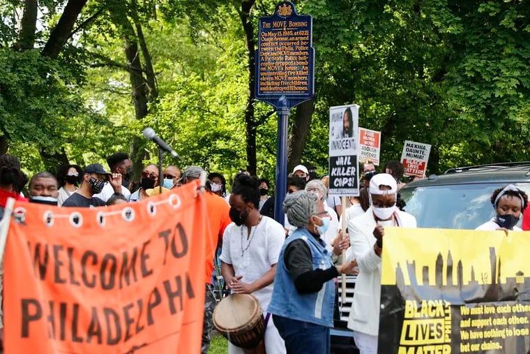 A crowd gather near a marker showing the MOVE Bombing location during a 36th anniversary remembrance march at Osage Avenue and Cobbs Creek Parkway in West Philadelphia on Thursday, May 13, 2021.
