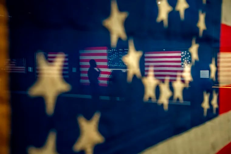 Staffers at the Museum of the American Revolution are reflected in the glass of a framed flag as they prepare an exhibition of historic flags that opened on Saturday, just in time for the nation’s patriotic season, which kicks off on Monday, Flag Day.