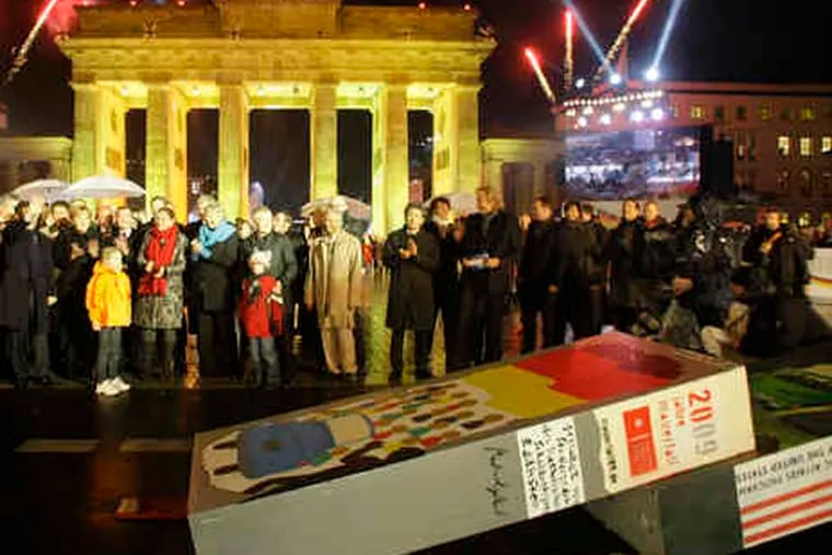 Twenty years ago, right, the Berlin Wall came down, to joyous celebrations. Above, dominoes lay on the ground yesterday in front of the Brandenburg Gate, symbolizing both the moment the wall came down and the fall of communist countries from Poland to Hungary to the Soviet Baltic states. At ceremonies yesterday, German Chancellor Angela Merkel called that day in 1989 &quot;one of the happiest moments of my life.&quot; Story, A2.