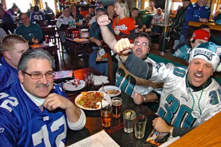 Eagles fans Larry Barnard and Rocco Ricccio (right) lead cheers for their team while across the table former neighbors and Giants fans Joe Zaczek Jr. and his son Joe III wait their turn. (Clem Murray / Staff Photographer)