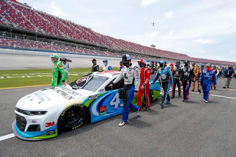 Nascar drivers Kyle Busch, left, and Corey LaJoie, right, join other drivers and crews as they push the car of Bubba Wallace to the front of the field prior to the start of the NASCAR Cup Series auto race at the Talladega Superspeedway in Talladega Ala.,