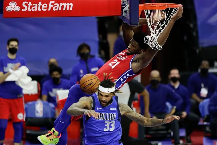 Sixers center Joel Embiid hangs on the rim after dunking the basketball over Mavericks center Willie Cauley-Stein.