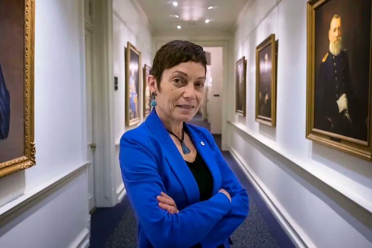Widener's 10th president, Julie E. Wollman, stands in the hallway outside of her office among the portraits of her predecessors. She is the first woman to lead the university.