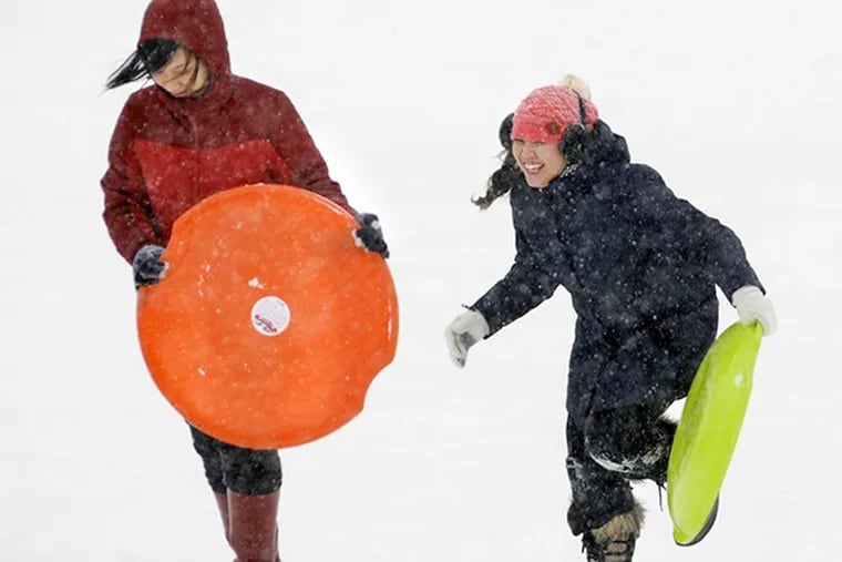 Ama Liew and Vivian Le, students at Massachusetts College of Pharmacy and Health Sciences University, enjoy sledding at Quinsigamond Community College in Worcester, Mass. on Thursday, Feb. 13, 2014.  They initially came to the hill with cardboard and garbage bags; they left and returned with these real sledding saucers.  (AP Photo/Worcester Telegram & Gazette, Christine Peterson)