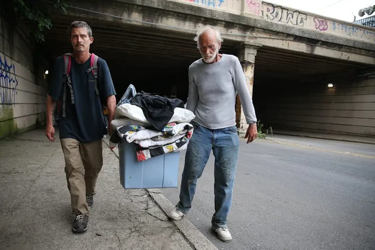Jason Carmine (left) and his father, Kevin, who were living under the Tulip Street bridge, carry away their belonging as police evicted people living at two of Kensington’s heroin camps.