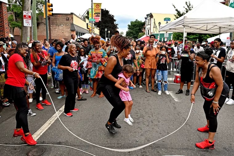 Vernell Prince with the 40+ Double Dutch Club of Philly and South Jersey takes 3 year-old Elijahrae Shuler-Colon from the audience to jump rope during the annual Odunde Festival on South Street Sunday.