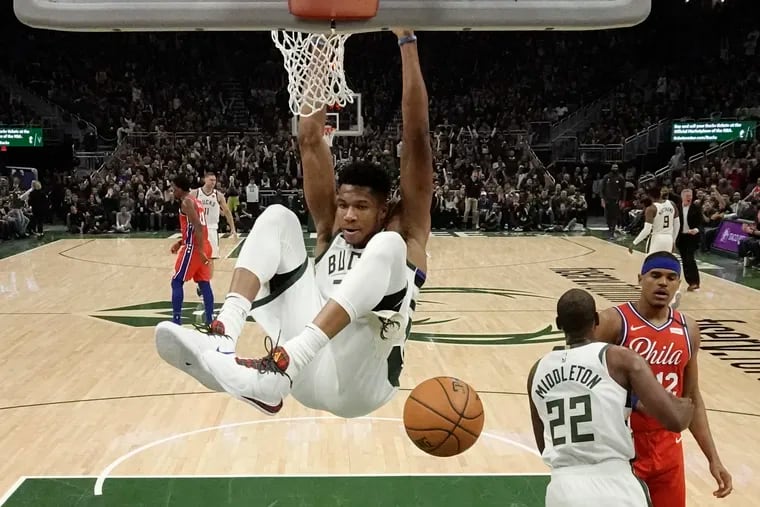 Milwaukee Bucks star Giannis Antetokounmpo hangs on the rim after throwing down a slam dunk during the first half against the Sixers.
