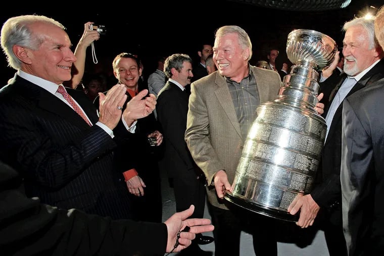 Flyers legends Bob Clarke (left) and Bernie Parent present the Stanley Cup to Ed Snider, who was Comcast Spectacor chairman, during a “finale party” at the Spectrum, the arena in South Philadelphia where the team started. Snider died earlier this year and his family has agreed to sell its remaining interest in the team to Comcast, which already is the majority owner.