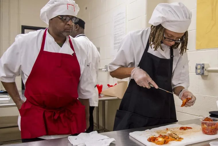 Anthony Cunningham (left), 53, a longtime professional chef, watches as Damon Roundtree, 18, a recent graduate of Philadelphia Learning Academy High School, cleans and cuts up roasted peppers at a training program conducted by hospitality union Unite Here at Strawberry Mansion High School.  Graduates of the program are guaranteed jobs in the restaurant industry.