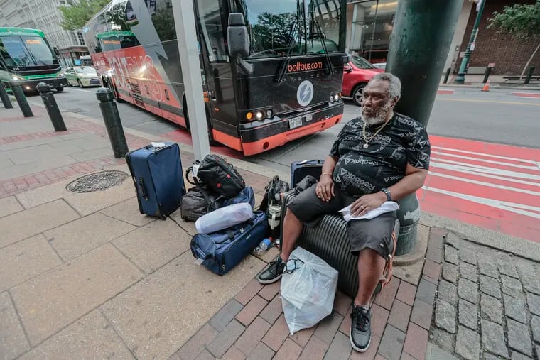 Andrea Smith, 69, from Oklahoma, sits on the sidewalk off of Market Street waiting for a bus in July. Travelers deserve a safe and accessible terminal, writes the Editorial Board, and the new Spring Garden Street location is not it.