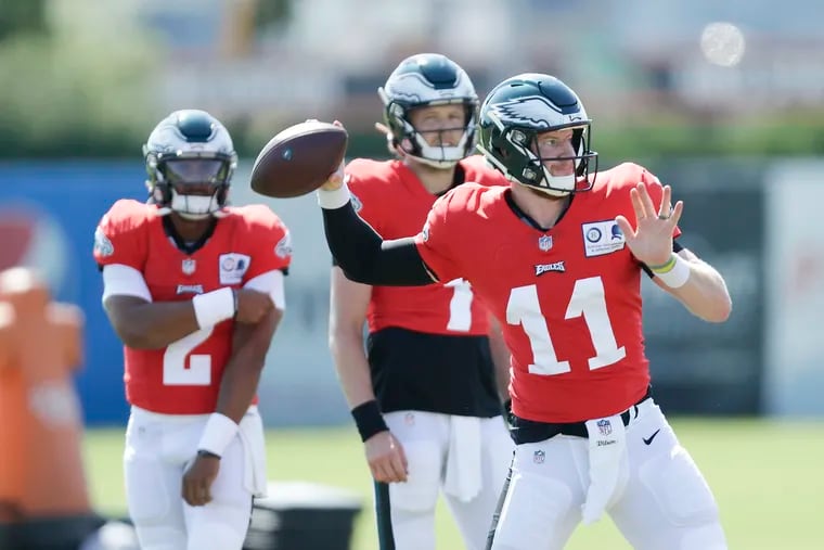 Eagles quarterback Carson Wentz (rigth) throws the football as backup quarterbacks Nate Sudfeld (center) and Jalen Hurts watch during training camp at the NovaCare Complex in South Philadelphia on Monday August 17, 2020.