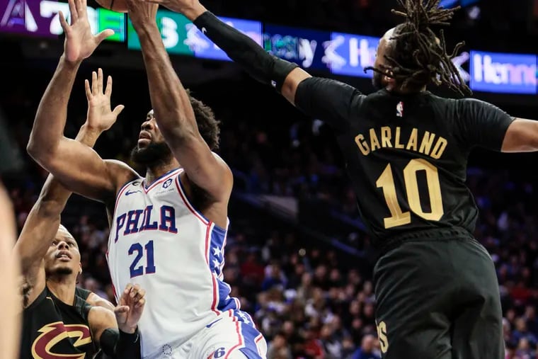 Sixers center Joel Embiid goes up for a shot between Cavaliers players Isaac Okoro (35) and Darius Garland (10).