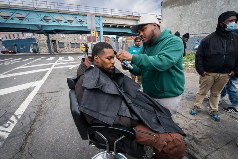 Barber Josh Santiago cuts the hair of Phillip Matthews on Friday. Santiago, a 33-year-old barber from Northeast Philadelphia, has been quietly giving haircuts on Kensington's side streets for years.