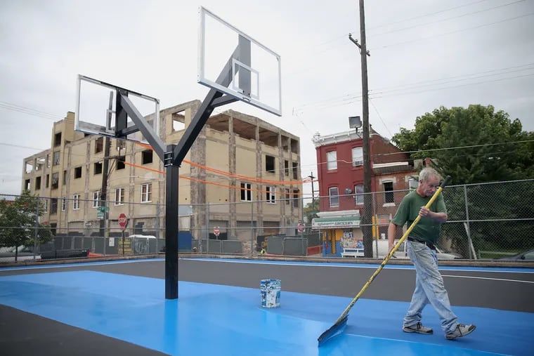 Cass Construction worker Joe Scheidly paints the newly renovated basketball court at the playground at Eighth and Cumberland streets in North Philadephia on Wednesday, June 27, 2018. The basketball court, renovated with the help of the Sixers Youth Foundation, was the site where 17-year-old Robert Reid was gunned down in 2014.