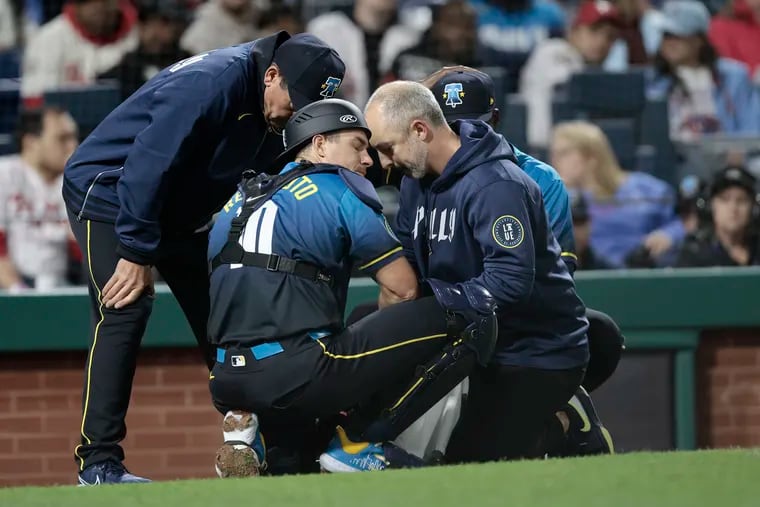 Phils assistant athletic trainer Joe Rauch, right, and manager Rob Thomson look at J.T. Realmuto’s forearm/wrist area after Realmuto was hit while catching for Yunior Marte on Friday.
