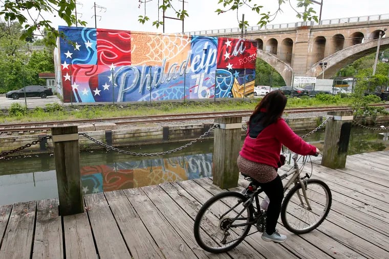 A bicyclist rides on the Manayunk Canal Path across from the new painted mural on the Michael's California Detailing building in Manayunk. The former mural, painted by Tish Ingersoll, was painted over without any advance notice.