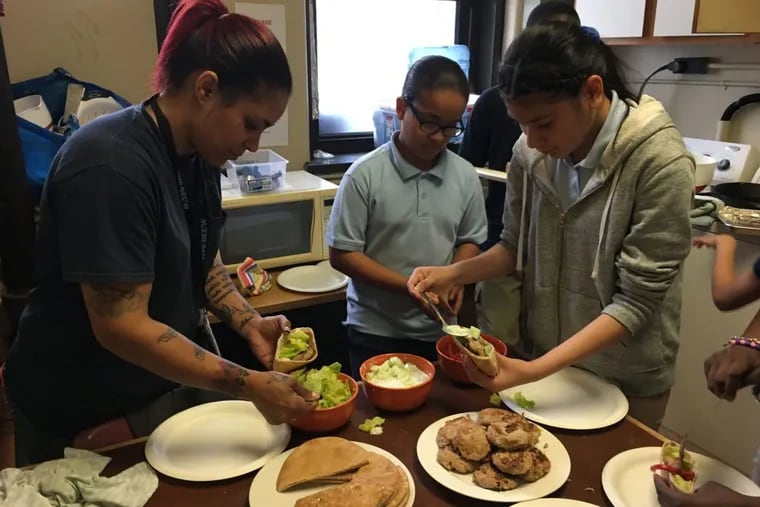 Juliana Marte (left), mother of cooking student Chris Marte, adds garnishes to her Greek turkey burger as Keisi Cedano and Yarethzy Campos prepare burgers for their guests at the last cooking class and party at Cramer Elementary School in Camden.
