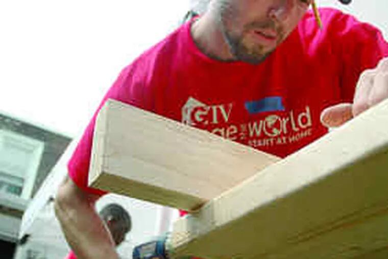VOLUNTEERING with HGTV's &quot;Change the World,&quot; a carpenter (above) yesterday helps renovate a 70-year-old Frankford rowhouse chosen for a makeover by the host, Carter Oosterhouse (right, chatting with another red-shirted volunteer). The facility, on the 4200 block of Romain Street, provides transitional housing for veterans.