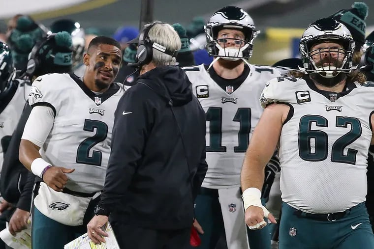Carson Wentz (11) ponders his future after Jalen Hurts (2), speaking with coach Doug Pederson, replaced him at Green Bay on Dec. 6, 2020. Center Jason Kelce (62) returned to the Eagles for 2021. Wentz forced a trade.