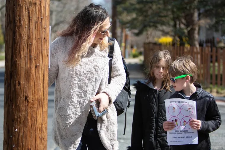 Erica Windisch and her kids, Adam, 7, and Lucy, 8, hang up fliers to promote social distancing in their Penn Wynne neighborhood in Montgomery County.
