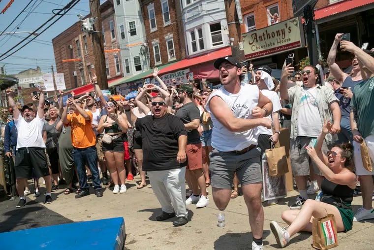 The crowd cheers as a group of men with Pace Roofing LLC compete in the grease pole contest at the South 9th Street Italian Market Festival in Philadelphia on Saturday, May 21, 2022. The festival return to 9th Street this weekend Saturday, May 18 and Sunday, May 19.