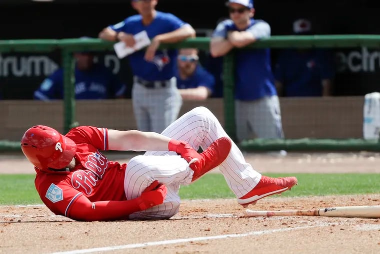 Philadelphia Phillies' Bryce Harper rolls on the dirt holding his leg after getting hit by a pitch against the Toronto Blue Jays during the sixth inning in a spring training baseball game, Friday, March 15, 2019, in Clearwater, Fla. Harper sustained a bruised right foot Friday, but manager Gabe Kapler said the team wasn't overly worries about the injury. Initial X-rays were negative, the team said, but Harper then left the ballpark for more detailed X-rays. (Yong Kim/The Philadelphia Inquirer via AP)