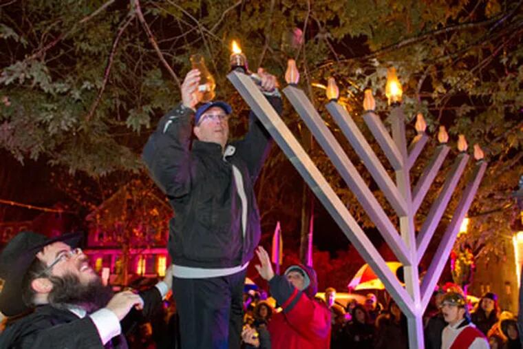 (Left) Rabbi Yitzchok Kahan steadies Paul Litwack, of Medford, as he lights a candle on the Menorah, makring the first night of Hanukah, in Tomlinson Park, Main St., Medford, December 20, 2011.  ( David M Warren / Staff Photographer ) EDITORS NOTE:  JHANUKAH21 126140 MEDFORD 122011 Chabad Lubavitch of Camden and Burlington Counties held a lighting of the Menorah to celebrate the first night of Hanukah.  1/