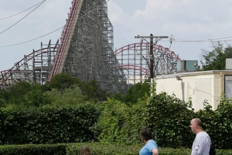 The Texas Giant roller coaster ride sits idle as people walk nearby looking from outside the Six Flags Over Texas park Saturday, July 20, 2013, in Arlington, Texas. Investigators will try to determine if a woman who died while riding the roller coaster at the amusement park Friday night fell from the ride after some witnesses said she wasn't properly secured.(AP Photo/LM Otero )