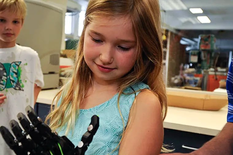 Third-grader Olivia Williamson, who was born without fingers on her left hand, tries on a prosthetic hand developed by a group of students at Plymouth Whitemarsh High School. ( RON TARVER / Staff Photographer )