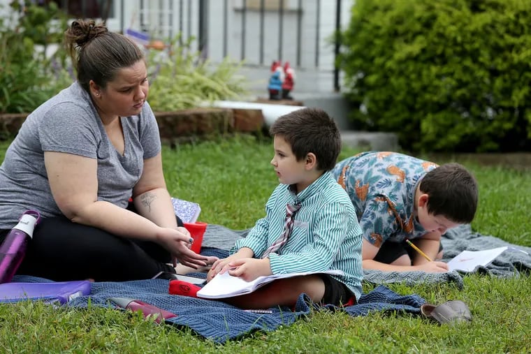 Elizabeth Dukart (left) talks with her son, Matthew, 6, (center), as Sam, 9, (right) works in the background during a homeschooling session on their lawn in Cherry Hill. Dukart pulled her kids from Cherry Hill public schools to homeschool them during the pandemic.