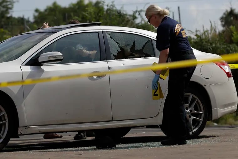 A Philadelphia Crime Scene investigator places an evidence marker near a shell casing found by a car involved in a homicide at a Global gas station on the 4600 block of Lancaster Avenue in West Philadelphia on Sunday, where a 19-year-old man was shot eight times.
