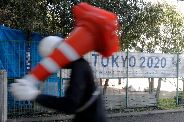 A worker on duty at a road construction site walks past a banner promoting the 2020 Olympic Games in Tokyo.