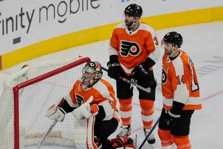 Flyers goalie Carter Hart takes the puck from the net after Vancouver's Alex Chiasson scored in the second period. Defenseman Keith Yandle and center Sean Couturier look on.