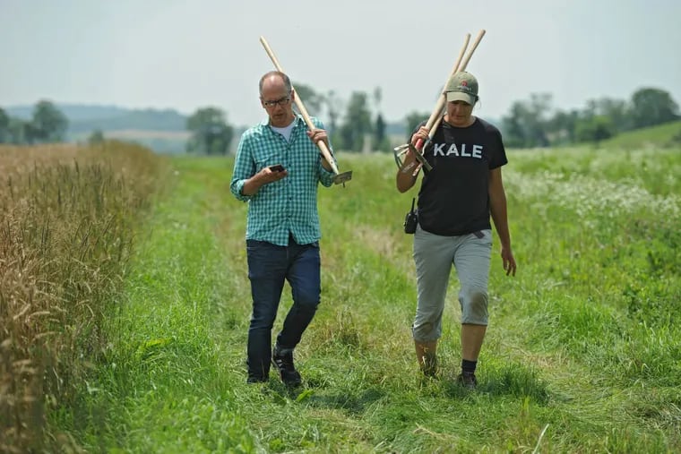 Jim Oseland (left), 52, the editor-in-chief of Rodale Press' Organic Life, with hoe in hand, checks his iPhone as he walks the fields with Cynthia James, 44, program manager at the Rodale Institute farm July 7, 2015.