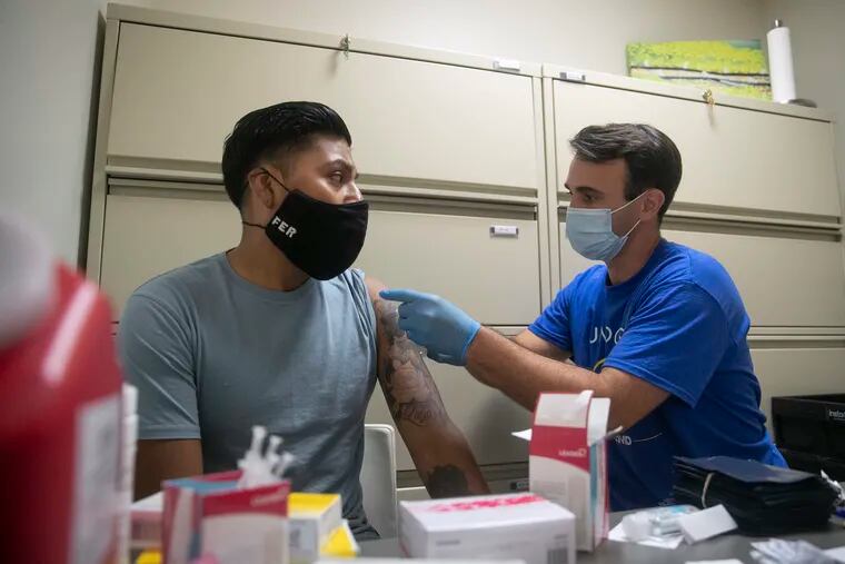 Jose Torradas of Unidos Contra COVID (right) places a band-aid on the arm of Fernando Rodriguez after giving him his first dose of the COVID-19 vaccine at Garces Laboratories in Old City on Saturday, July 17. Vaccination rates among the city's Hispanic population have been quickly improving.