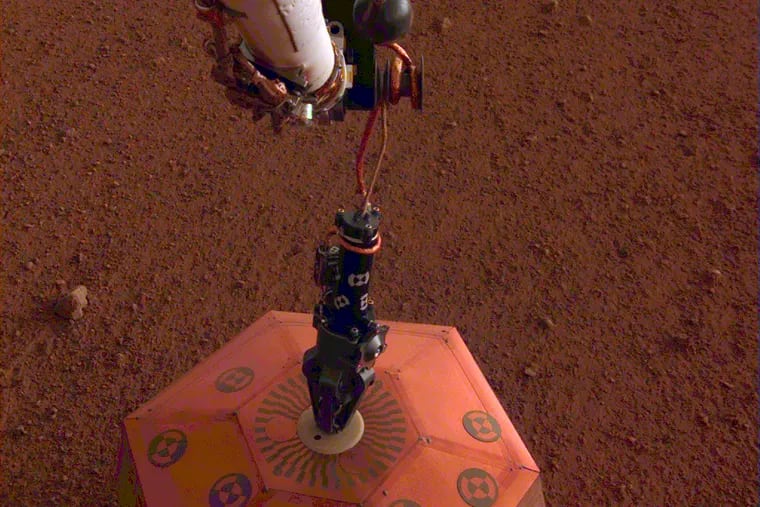 This photo provided by NASA Jet Propulsion Laboratory, shows the new Mars lander placing a quake monitor on the planet’s dusty red surface.  The unprecedented milestone occurred less than a month after Mars InSight’s touchdown. InSight’s robotic arm removed the seismometer from the spacecraft deck and set it directly on the ground Wednesday, Dec. 19, 2018 to monitor Mars quakes.(NASA Jet Propulsion Laboratory via AP)