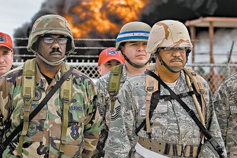 With a flame raging at the Fire Training Pit, Master Sgt. William Price (left) of Eastampton stands at ease with other soldiers at a runway repair training site. (DAVID M WARREN / Staff Photographer)
