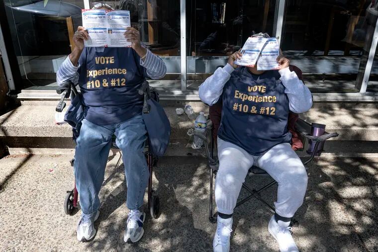 Two unidentified volunteers covered their faces with pamphlets as they give them out to voters outside the Fleisher Art Memorial election polling place, in South Philadelphia.