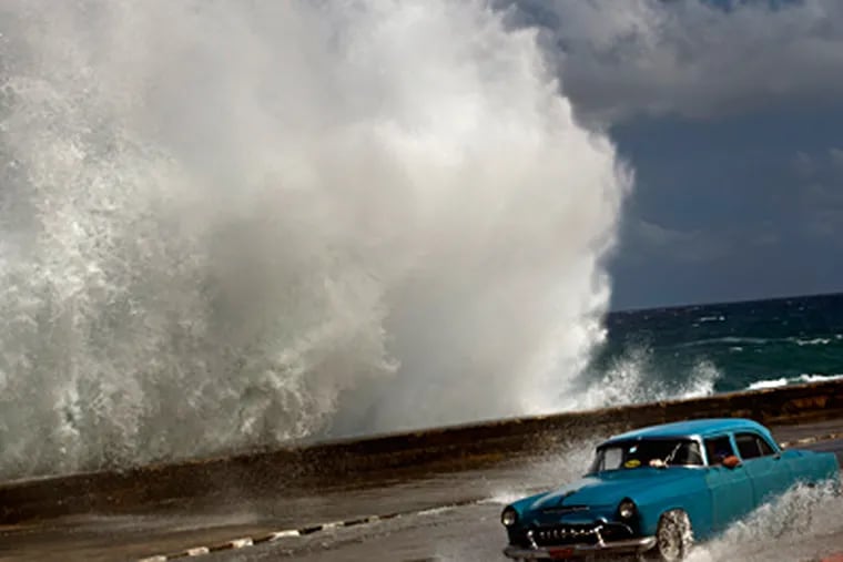 A driver maneuvers along a wet road as a wave crashes against the Malecon in Havana, Cuba, on Thursday after Hurricane Sandy blasted across eastern Cuba. RAMON ESPINOSA / Associated Press