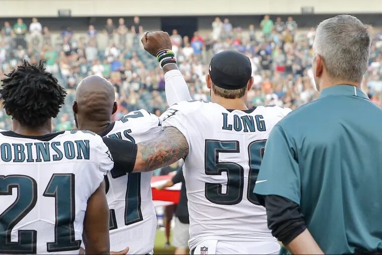 Eagles strong safety Malcolm Jenkins has his fist raised as Eagles teammate defensive end Chris Long drapes his arm around him during the national anthem Thursday night.