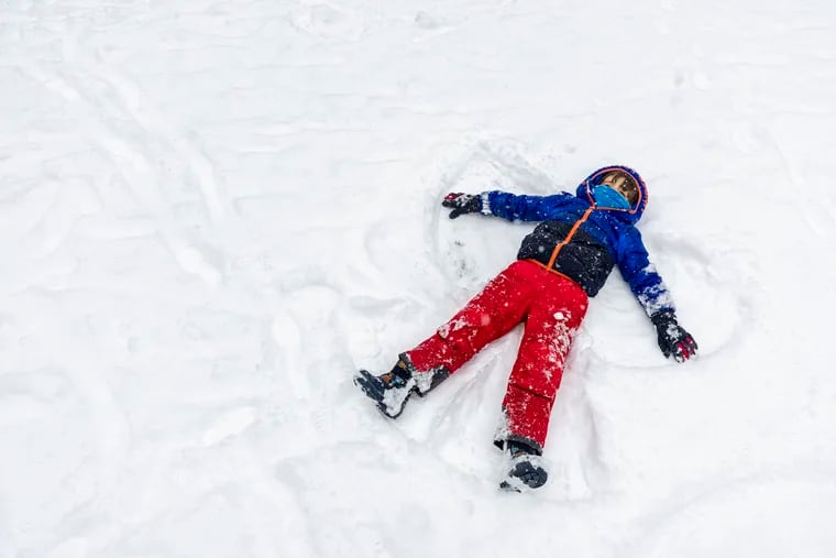 Arlo Dalili, 5, makes snow angels on the ground while out with his mother, Jennifer Breslow, of Rittenhouse. The Philadelphia School District had a traditional snow day Friday.