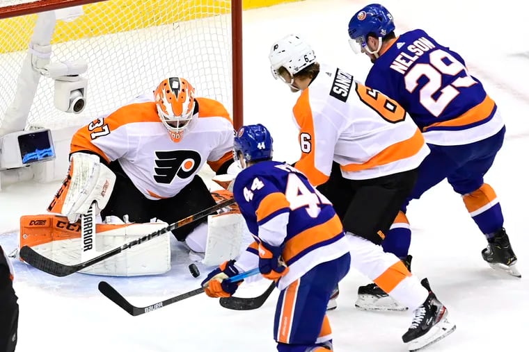 Flyers goaltender Brian Elliott makes a save as Flyers defenseman Travis Sanheim (6) and New York Islanders' Jean-Gabriel Pageau (44) and Brock Nelson (29) battle for position during the first period Sunday.