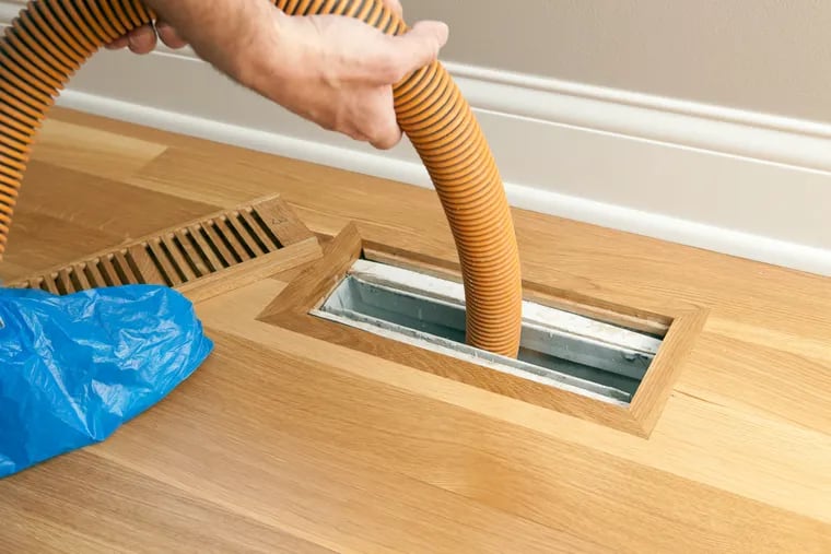 A worker is using a vacuum to clean a vent and duct. The EPA says that ductwork cleanings provide no measurable benefit for homeowners, even if residents suffer from allergies or asthma.