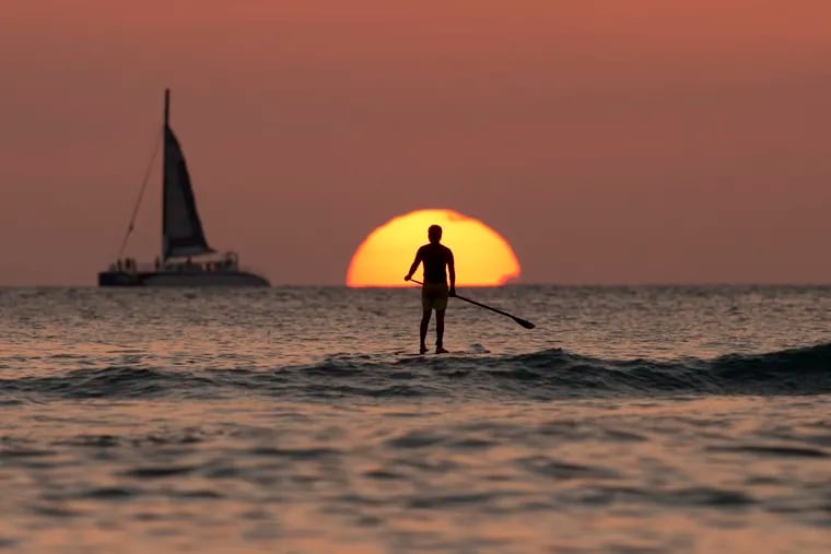 FILE – In this Dec. 31, 2013, file photo, a paddleboarder looks our over the Pacific Ocean as the sun sets off of Waikiki Beach, in Honolulu.