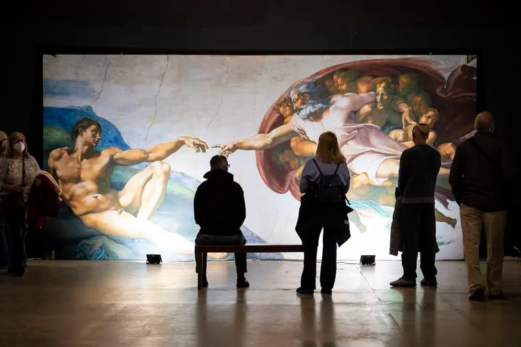 Visitors take in "The Creation of Adam" at Michelangelo's Sistine Chapel exhibition at the Fashion District in Philadelphia, Pa. on Wednesday, January 26, 2022.  The 2-story exhibit features recreations of Michelangelo's Sistine Chapel ceiling frescos and the Last Judgement.