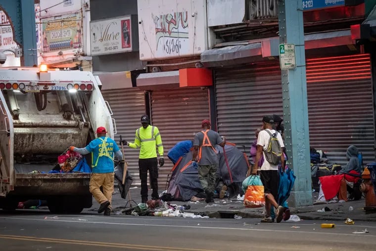 Sanitation workers clear a trash-strewn encampment along Kensington Avenue last week.