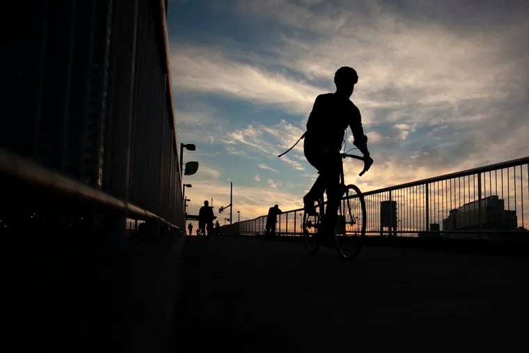 People are silhouetted as they bike and walk down the ramp to the Schuylkill River Trail underneath the South Street Bridge in Philadelphia.