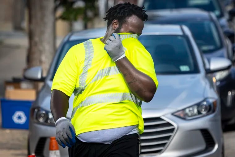 Quamir Anderson wipes sweat from his face as he walks along Wolf Street in South Philadelphia collecting the weekly trash during the heat wave on July 21. It was a hot month for sanitation workers.